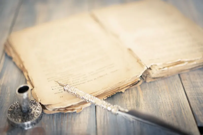 Un libro antiguo abierto junto a una pluma y un tintero